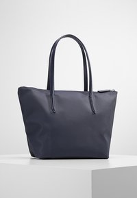 Navy tote bag with a structured shape, made of textured material. Features two long handles and a zip closure. Simple design, no visible hardware.