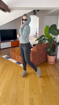 Helehelesinine kapuutsiga dressipluus, mustad kitsad teksad ja hallid pahkluu saapad. Taustal on taim ja diivan tekstuuriga kangast.