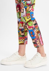 Witte sneakers met een soepel leren afwerking en een gestructureerde rubberen zool, gecombineerd met kleurrijke cropped broek met een strippenmotief en ritsen.