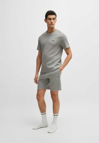 Graues kurzärmliges T-Shirt und Shorts-Set aus strukturiertem Stoff, mit kleinem schwarzem "BOSS"-Logo auf der Brust und am Bein. Weiße Socken mit schwarzen Akzenten.