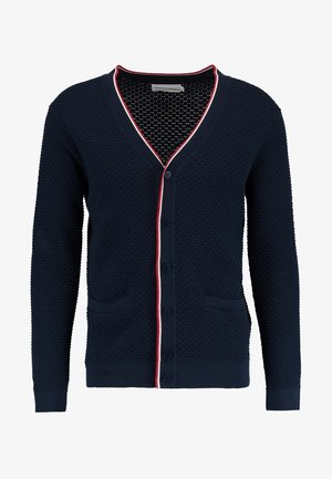 Navy cardigan with a textured honeycomb pattern, red and white trim along the V-neck and button placket, two front pockets.