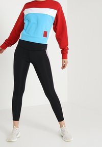 Color-blocked sweatshirt in red, white, and light blue; paired with black leggings featuring pink side stripes and white sneakers.