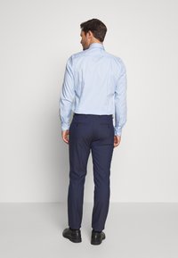 Ljusblå rutig skjorta med krage, kombinerad med mörkblå byxor. Svarta skor synliga; fokuserat på bakvyn av outfiten.