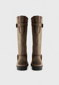 Bottes marron hautes en suède, présentant des accents en cuir contrastants, des coutures verticales, un détail de boucle et une semelle en caoutchouc noir texturé.