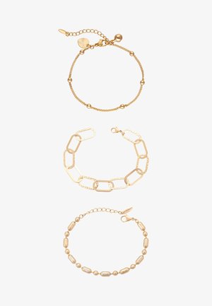 Trzy złote bransoletki: koralikowy łańcuch z małymi okrągłymi zawieszkami, duży prostokątny łańcuch ogniw oraz teksturowana bransoletka z owalnymi i okrągłymi koralikami.