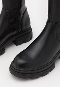 Czarne skórzane botki za kostkę z gładkim wykończeniem, masywną gumową podeszwą i zamkiem błyskawicznym z boku. Posiadają zaokrąglony nos i minimalne detale szewne.