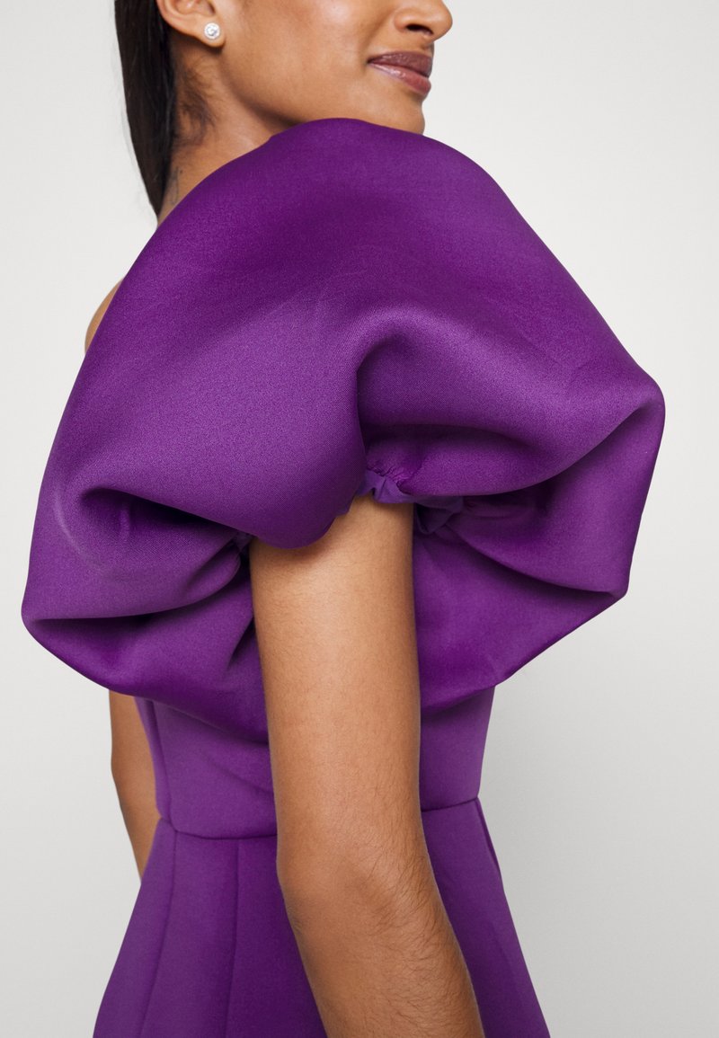 Fioletowa sukienka z wyraźnym, obszytym detalem na ramionach, wykonaną z gładkiego materiału, o dopasowanym kroju i subtelnym marszczeniu.