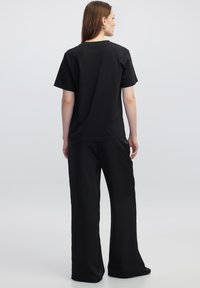 Camiseta de algodón negra de corte relajado y mangas cortas, combinada con pantalones negros holgados, vista desde atrás. Diseño sencillo, sin patrones.