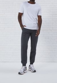 Camiseta blanca de manga corta combinada con pantalones de chándal gris oscuro y zapatillas plateadas. El conjunto tiene un corte relajado y un diseño simple.