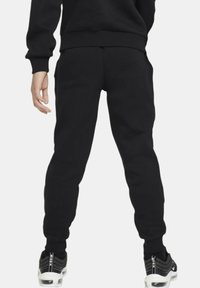 Pantalones de chándal negros de algodón con tobillos ajustados y bolsillos laterales, combinados con deportivas en negro y blanco. Textura suave y corte relajado.