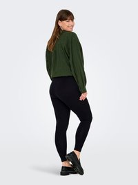 Camicia verde corta con una finitura testurizzata, leggings neri e scarpe chunky nere. La camicia ha una chiusura frontale con bottoni e maniche arrotolate.