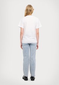 Hvit bomulls T-skjorte med korte ermer, kombinert med lyseblå denimjeans. Jeansene har rett passform og er litt falmede. Svarte støvler fullfører antrekket.