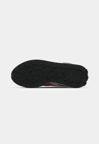 Black sneaker sole with circular rubber tread patterns and a textured finish. Features red, gray, and white accents along the sides.