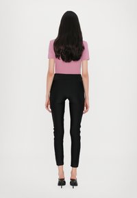 Pantaloni neri aderenti con una vita alta, abbinati a una maglietta corta rosa, visti da dietro. I capelli scendono dritti fino a metà schiena.