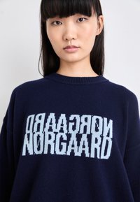 Maglione oversize blu navy realizzato in materiale lavorato a maglia, con una grande grafica testuale azzurro chiaro "NORGAARD" sulla parte anteriore.
