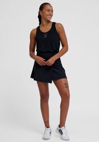 Svart atletisk tanktopp med en subtil chevrondesign, kombinert med en matchende svart skjørt. Glatt stofftekstur, moderne passform.