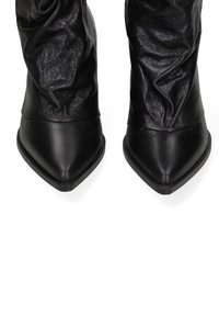 Stivaletti in pelle nera con un design morbido, punta affusolata e texture liscia. Presentano una suola spessa per stabilità e supporto.