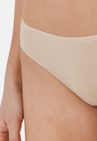 Beżowe, paskowane majtki bikini o gładkiej strukturze i miękkim, elastycznym pasku w talii. Krój jest niski, zaprojektowany dla wygody i zakrycia.