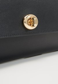 Czarna skórzana torebka z zapięciem na złotą kłódkę, o gładkiej fakturze i prostych liniach, podkreślająca nowoczesny i minimalistyczny design.