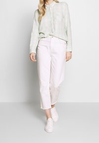 Camisa de cuadros verde claro con botones, jeans blancos cortos con bajo deshilachado y zapatillas blancas. La camisa tiene un bolsillo frontal y mangas largas.