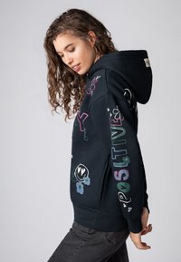 Zwarte hoodie met kleurrijke grafische ontwerpen, waaronder bloemen en tekst. Beschikt over een voorvak en een capuchon met trekkoord. Zachte textuur.