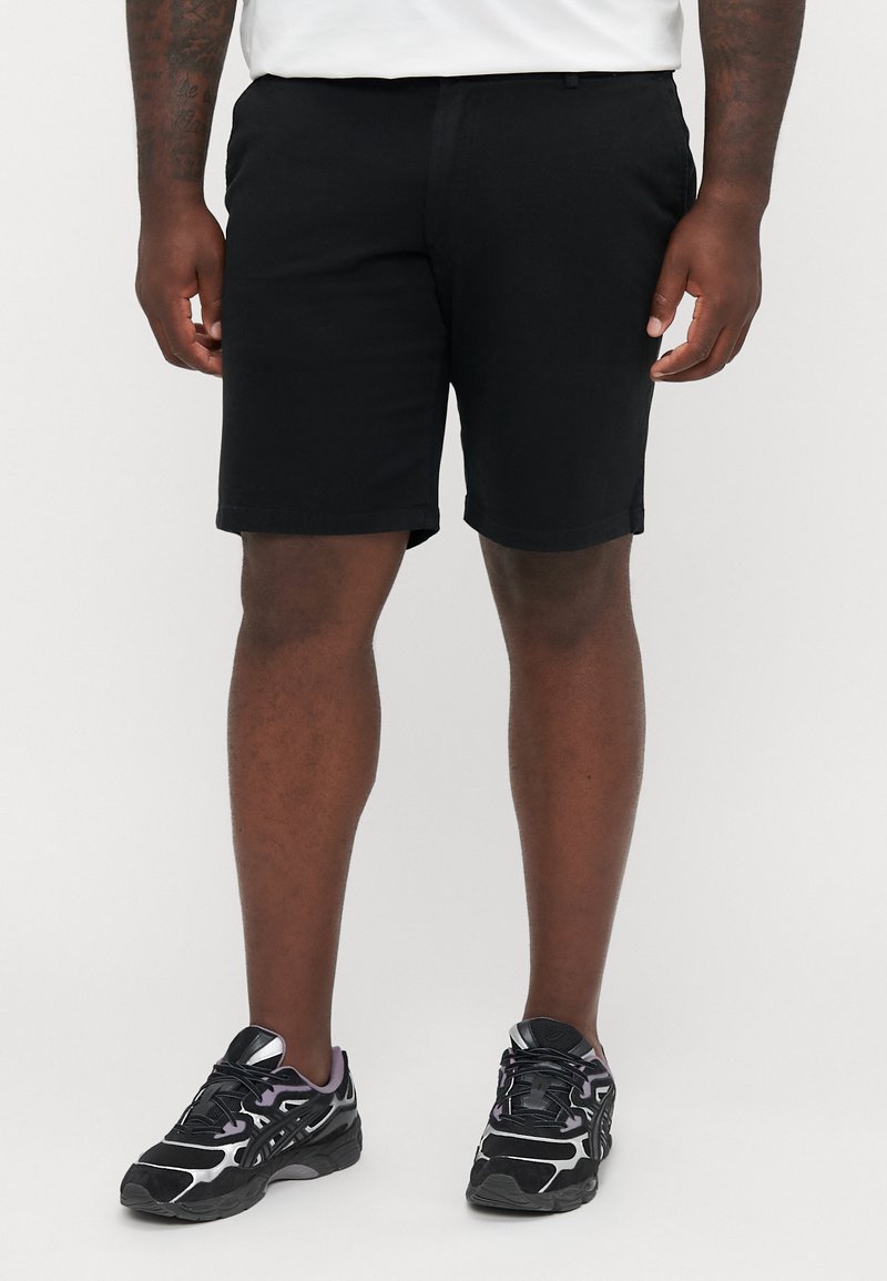 Sorte shorts med en rett kutt, laget av et glatt stoff og med rullede kanter, kombinert med sorte treningssko med sølvdetaljer.