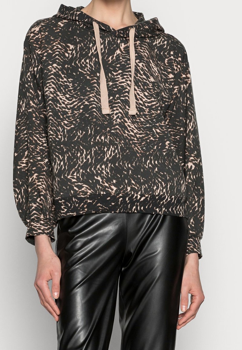 Sudadera con capucha de patrón negro y marrón, de corte relajado, con tejido suave, cordones beige y puños acanalados. Combinada con pantalones negros brillantes.