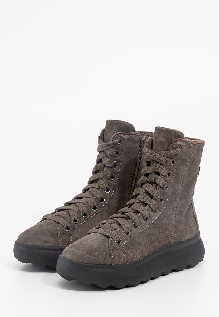 Hochformatige graue Wildlederstiefel mit schwarzen Gummisohlen, Frontschnürung und seitlichen Reißverschlüssen, vor einem weißen Hintergrund gezeigt.