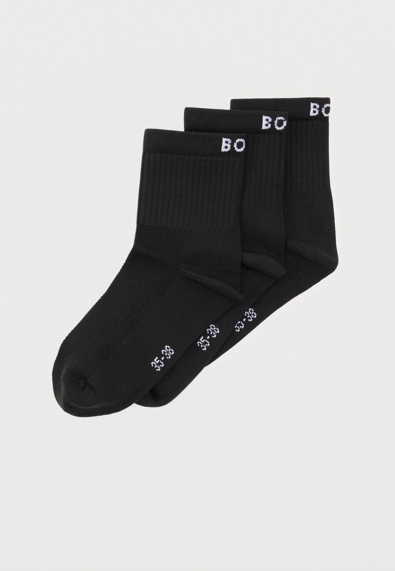 Trois paires de chaussettes noires montant jusqu'à la cheville avec des bords côtelés et des marquages de taille blancs sur la semelle et le bord, disposées en chevauchement sur un fond blanc.