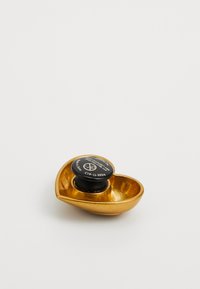 Gold heart-shaped decorative item with a black round base, featuring a label visible on top and smooth metallic texture.