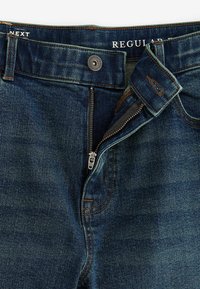 Donkerblauwe jeans van denim met een normale tailleband, voorzien van een ritssluiting, koperen stiksels en een logo-label aan de binnenkant van de tailleband.