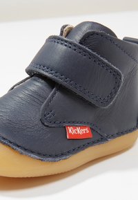 Ciemnoniebieskie skórzane buty dziecięce z zapięciem na rzep, gumową podeszwą i czerwonym logo "Kickers". Z ozdobnymi szwami i zaokrąglonym noskiem.