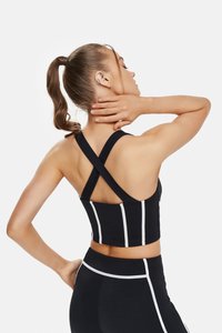 Black activewear crop top with crossed straps, featuring white horizontal stripes along the sides. Smooth, stretchy fabric with a fitted design.