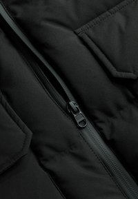 Jachetă izolată neagră cu fermoar frontal, prevăzută cu buzunare plate și o textură solidă, netedă. Fermoar și cusături în negru asortat.