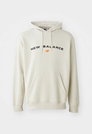 Light beige hoodie with drawstring hood, front pocket, and black "NEW BALANCE" text. Soft fabric with ribbed cuffs and hem.