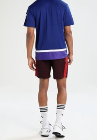 Sportkläder som består av en blå kortärmad skjorta, röda och maroon shorts samt vita randiga strumpor i kombination med svarta sportskor.