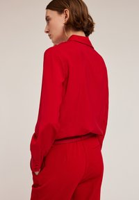 Rode blouse met lange mouwen van lichtgewicht stof, voorzien van een kraag en knoopmanchetten, gecombineerd met bijpassende hooggestrikte broeken.