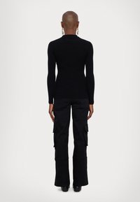 Μαύρη ριπ ψηλή μπλούζα με μακριά μανίκια και στενή εφαρμογή, συνδυασμένη με μαύρο παντελόνι cargo ψηλής μέσης με πλάγιες τσέπες. Μαύρες μπότες με τακούνι.