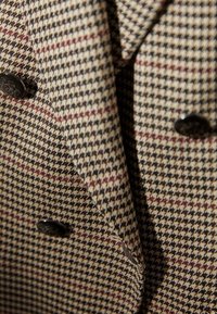 Manteau croisé avec boutons noirs présentant un motif pied-de-poule beige, marron et bordeaux en gros plan.
