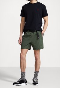 Svart bomullströja och gröna shorts. Shortsen har ett bälte, medan outfiten matchas med svarta sneakers och grå mönstrade strumpor.