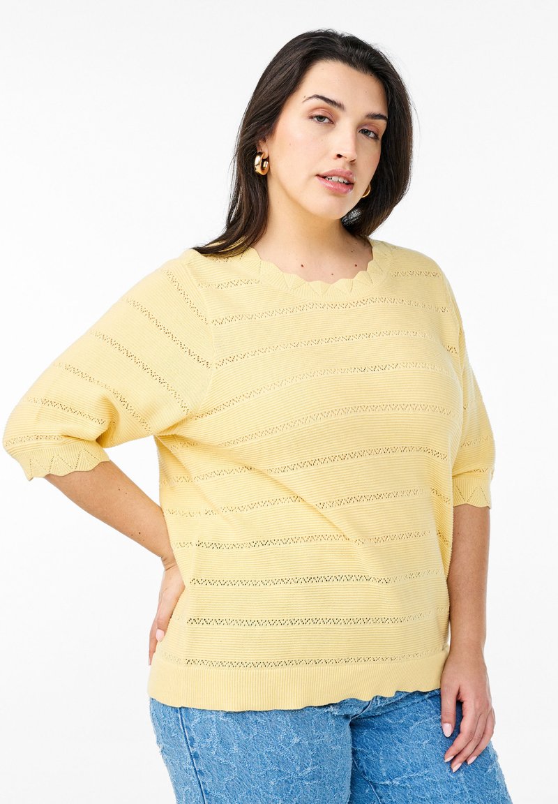 Pull en tricot jaune avec un col festonné, des rayures horizontales et des manches courtes bouffantes. Il présente un motif ajouré et une finition texturée.