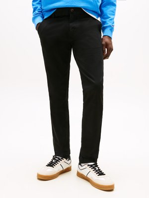 Black chinos with a slim fit, featuring side pockets and a button closure, paired with white and black sneakers with gum soles.