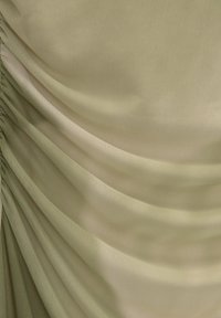 Tissu vert clair avec une finition texturée, présentant un drapé froncé qui crée des plis doux et une profondeur de surface variée.