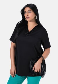 Top negro de manga corta con un escote en V texturizado y adornos de lentejuelas, combinado con pantalones color teal y un bolso negro con flecos.