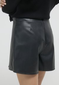 Shorts en cuir noir avec une texture lisse, dotés d'une fermeture arrière à zip et de lignes épurées et ajustées.