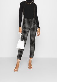 Black ribbed turtleneck, check-patterned tailored pants in black and white, white strappy sandals, and a small white handbag.