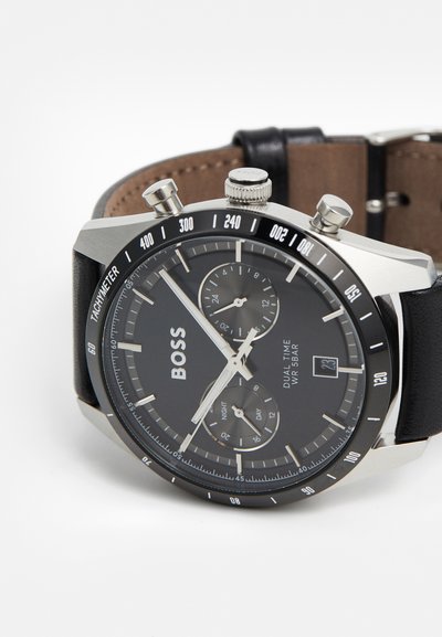 Montre avec bracelet en cuir noir, boîtier en acier inoxydable argenté, cadran noir, affichage double fuseau horaire, échelle tachymétrique et trois sous-cadrans chronographes.
