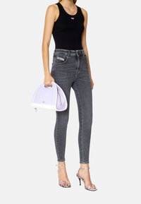 Jeans de talle alto grises, top negro sin mangas, bolso estructurado lila con base blanca y sandalias plateadas de tacón con tiras.