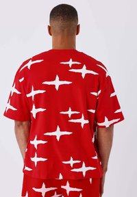 Rode shirt met korte mouwen, versierd met een gedurfde witte sterrenpatroon. Gemaakt van zachte stof, heeft het een ontspannen pasvorm en een ronde halslijn.