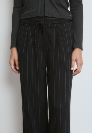 Pantalones de rayas negras fabricados con tela suave; cuentan con cintura ajustable con cordón, diseño de pierna ancha y sutiles rayas doradas sobre un fondo oscuro.